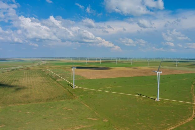 An aerial view of a solar panel farm next to a wind turbine farm in a rural area, with rows of brand new modern electric vehicles parked below.  The vehicles are neatly aligned along a new highway system.