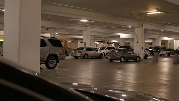 A photograph depicting a large parking lot at a car dealership, but nearly empty. There are only a few cars visible, and a sign in the background indicates 