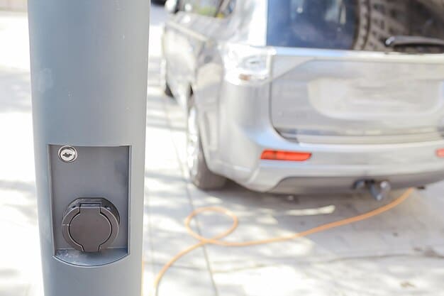 A close-up shot of an electric vehicle's charging port with a charging cable plugged in. The vehicle is parked in a residential driveway, highlighting the ease of charging at home.