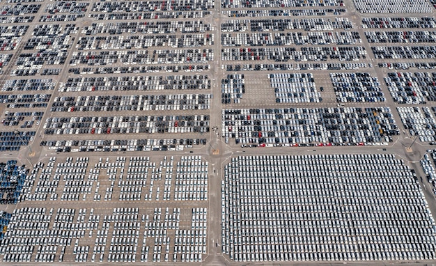 Aerial view of a large electric vehicle manufacturing plant in the Midwest, USA. Solar panels on factory roofs. Wide parking lot filled with electric vehicles awaiting shipment. Green landscaping around the facility. Bright, sunny day.