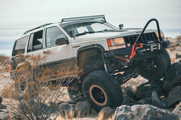 A Jeep Grand Cherokee navigating steep, rocky terrain, showcasing the capability of its air suspension system. The wheels are articulated, and the chassis is lifted to clear a large rock.