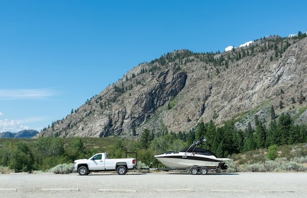 2025 Cadillac Escalade pulling a large boat trailer on a sunny day, showcasing its towing capabilities. The boat is securely attached, and the scenery includes a lakeside background with trees and clear skies.