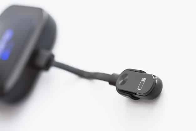 Close-up of the Hyundai Kona Electric's charging port with the charging cable plugged in. The background is intentionally blurred to focus on the details of the port and electrical connections. A faint outline of the Kona Electric's body is visible in the background.